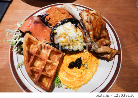 close up of an English full all day breakfast with truffle scrambled eggs, waffle, smoke salmon, mushroom with cheese and egg and stir fried chicken fillet and salad vegetables 125039116