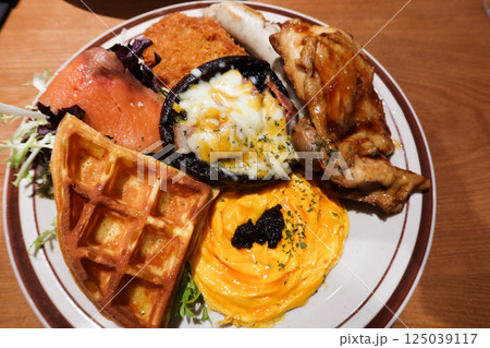 close up of an English full all day breakfast with truffle scrambled eggs, waffle, smoke salmon, mushroom with cheese and egg and stir fried chicken fillet and salad vegetables 125039117