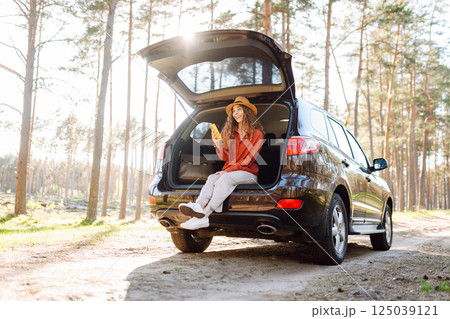 Beautiful woman sits in the trunk of a car outdoor and uses a smartphone. Lifestyle Beautiful woman sits in the trunk of a car outdoor and uses a smartphone. Lifestyle 125039121