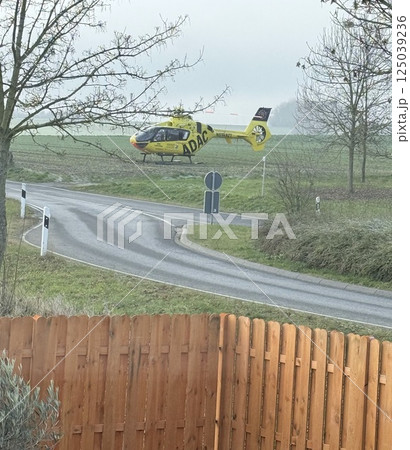 Orange helicopter on a green meadow with yellow flowers preparing to take off. No people. Sunny summer day. 125039236