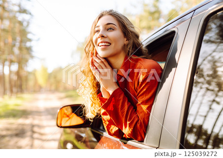 Young woman leaning out of the car window enjoying nature. Road trips summer holidays. 125039272