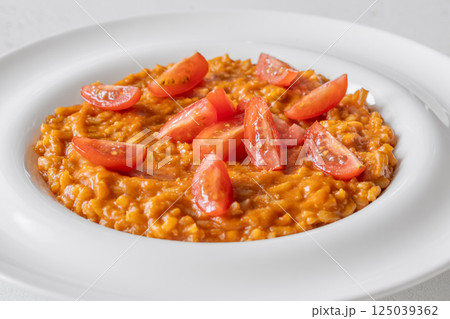 Creamy tomato risotto topped with cherry tomatoes on clean white plate Creamy tomato risotto topped with cherry tomatoes on clean white plate 125039362