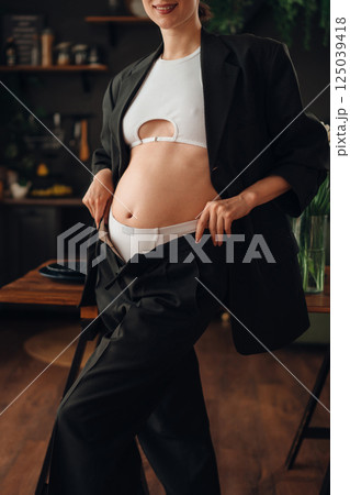Pregnant young woman posing in stylish outfit at home during daytime Pregnant young woman posing in stylish outfit at home during daytime 125039418