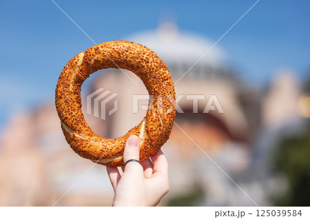 A hand holds a sesame simit outdoors in front of a mosque on a sunny day. A hand holds a sesame simit outdoors in front of a mosque on a sunny day. 125039584