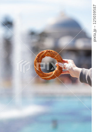 A hand holds a sesame simit outdoors in front of a mosque on a sunny day. A hand holds a sesame simit outdoors in front of a mosque on a sunny day. 125039587