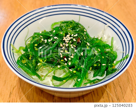 Bright Green Wakame Salad in Blue and White Bowl on Wooden Table with Sesame Seeds Bright Green Wakame Salad in Blue and White Bowl on Wooden Table with Sesame Seeds 125040283