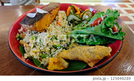 Delicious Fried Rice with Crispy Fried Salmon and Fresh Salad on Red Plate, Captured on Wooden Table in Cozy Restaurant Delicious Fried Rice with Crispy Fried Salmon and Fresh Salad on Red Plate, Captured on Wooden Table in Cozy Restaurant 125040289