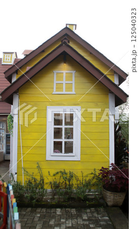 Charming Yellow Wooden House Facade with White Trim and Rustic Window, Surrounded by Lush Greenery in a Quaint Village Setting Charming Yellow Wooden House Facade with White Trim and Rustic Window, Surrounded by Lush Greenery in a Quaint Village Setting 125040323