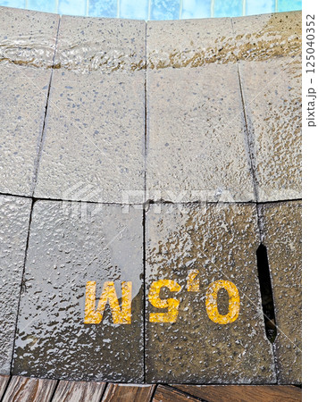Yellow depth information 0.5 M painted on wet stone tiles at the edge of a pool with blue water. Yellow depth information 0.5 M painted on wet stone tiles at the edge of a pool with blue water. 125040352