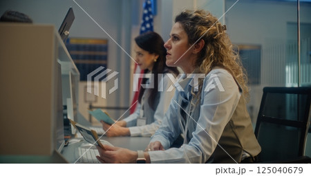 Female Airline Agents Checking Documents and Airplane Tickets of Passengers, Working on Computers 125040679