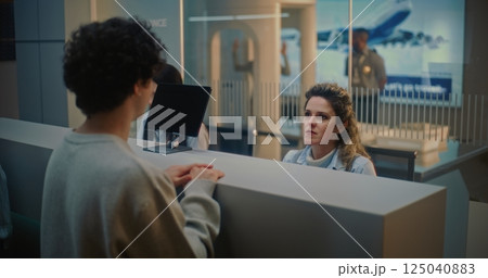 Airport Check-in Counter: Female Airline Worker Talking to Young Man During Passport Check 125040883