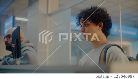 Young Man Verifying by Facial Recognition, Talking to Airline Worker During Passport Check 125040987