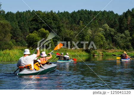 Family with children on rafting trip in Group kayak trip of different ages, adults, elderly. Rowing boat on the river, a water hike, summer adventure. 125041120