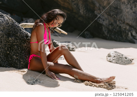 Smiling woman in a bikini sitting on sunny sandy beach, summer vibes Smiling woman in a bikini sitting on sunny sandy beach, summer vibes 125041205