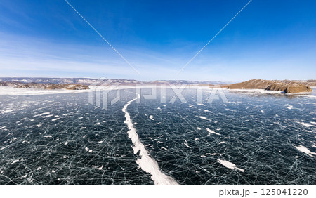 Aerial top view to Blue clear ice lake Baikal. Crack covered snow on frozen water surface. Cold winter landscape with mountains, sunny day, Natural background. Small Sea, Olkhon Gate, Russia, Siberia. Aerial top view to Blue clear ice lake Baikal. Crack covered snow on frozen water surface. Cold winter landscape with mountains, sunny day, Natural background. Small Sea, Olkhon Gate, Russia, Siberia. 125041220