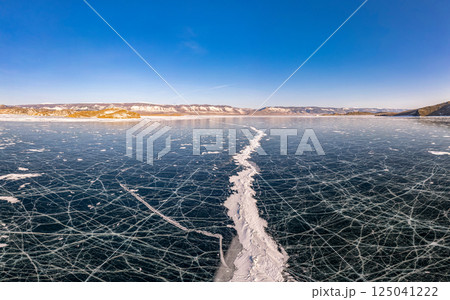 Aerial top view to Blue clear ice lake Baikal. Crack covered snow on frozen water surface. Cold winter landscape with mountains, sunny day, Natural background. Small Sea, Olkhon Gate, Russia, Siberia. 125041222