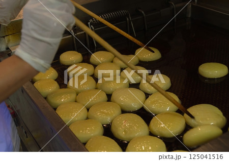 A chef skillfully frying golden dough balls in hot oil, creating a delicious culinary delight. A chef skillfully frying golden dough balls in hot oil, creating a delicious culinary delight. 125041516