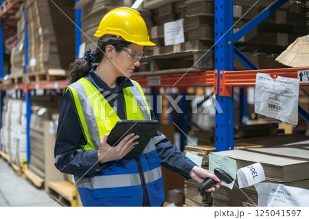 A worker scanning inventory in a warehouse using a tablet and barcode scanner, showcasing modern logistics. 125041597