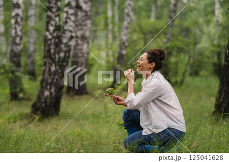 Woman eating wild strawberry sitting on grass in summer forest. Female enjoying nature, healthy lifestyle and simple life outdoors in rural environment Woman eating wild strawberry sitting on grass in summer forest. Female enjoying nature, healthy lifestyle and simple life outdoors in rural environment 125041628
