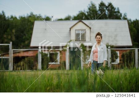 Woman standing with bouquet of blooming flowers in rustic backyard in summer. Female living simple natural life surrounded by nature and tranquility Woman standing with bouquet of blooming flowers in rustic backyard in summer. Female living simple natural life surrounded by nature and tranquility 125041641