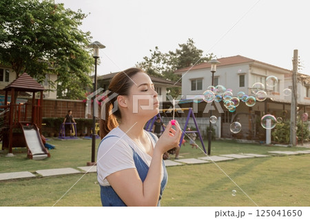 A woman blowing bubbles in a sunny park, enjoying a playful moment in a vibrant outdoor space. 125041650