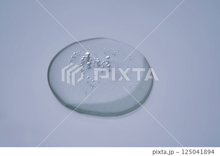 Textured round drop of serum with bubbles on dark blue background. 125041894