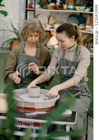 Mentor teaches pottery fundamentals, demonstrating sculpting skills on an electric wheel Active aging concept, retired woman explores pottery as a new passion using a spinning wheel Mentor teaches pottery fundamentals, demonstrating sculpting skills on an electric wheel Active aging concept, retired woman explores pottery as a new passion using a spinning wheel 125041999
