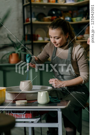 Young woman firing ceramic cup with gas torch at pottery workshop. Professional potter demonstrating firing technique with handheld torch 125042001