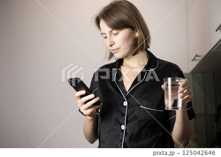 woman holding a glass of water and looking at her phone woman holding a glass of water and looking at her phone 125042646