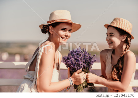 A woman and a child are sitting on a bench in a field of purple flowers lavande. The woman is holding a bouquet of flowers and the child is holding a bouquet of flowers as well A woman and a child are sitting on a bench in a field of purple flowers lavande. The woman is holding a bouquet of flowers and the child is holding a bouquet of flowers as well 125043170