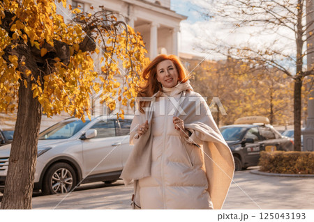 Woman Autumn City Street Fashion: Stylish redhead strolls, enjoying fall foliage near urban buildings. Woman Autumn City Street Fashion: Stylish redhead strolls, enjoying fall foliage near urban buildings. 125043193