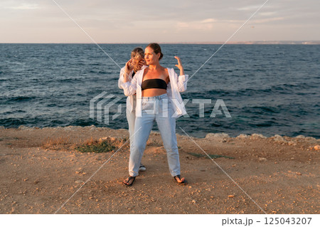 Women Friends Beach Sunset Pose - Two friends pose together by the sea at sunset. 125043207