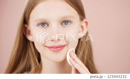 Close-up portrait of smiling young girl using cotton pad in studio on pink background. Adorable Caucasian girl using cotton round cleansing skin. Concept of skin care advertising for teens. Copy space Close-up portrait of smiling young girl using cotton pad in studio on pink background. Adorable Caucasian girl using cotton round cleansing skin. Concept of skin care advertising for teens. Copy space 125043232