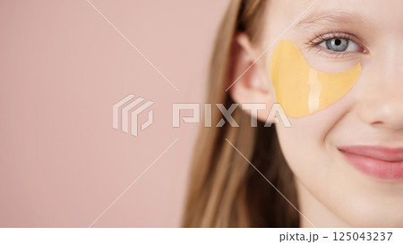 Happy cute young girl with eye patch on studio pink background. Half face portrait of blonde girl gen Alpha smiling looking at the camera. Concept of cosmetics advertisement for teenagers. Copy space 125043237