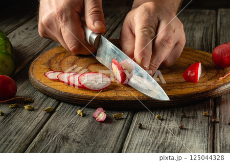Hands skillfully slice crisp radishes on a wooden cutting board. Bright colors and textures highlight a fresh salad preparation. Sunlight streams in, enhancing the atmosphere Hands skillfully slice crisp radishes on a wooden cutting board. Bright colors and textures highlight a fresh salad preparation. Sunlight streams in, enhancing the atmosphere 125044328