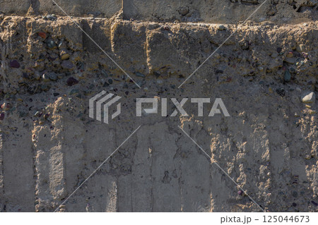 Weathered Cheap Uneven Concrete Surface with Pebbles under tangential harsh light 125044673