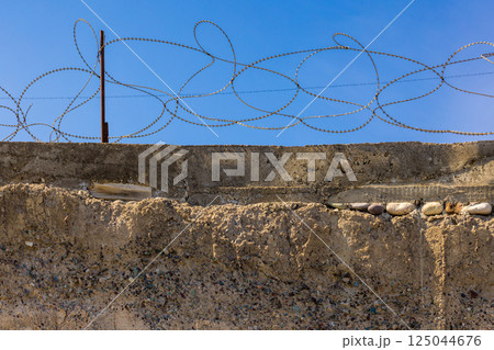 Concrete wall with barbed wire against a clear blue sky. Security barrier. 125044676