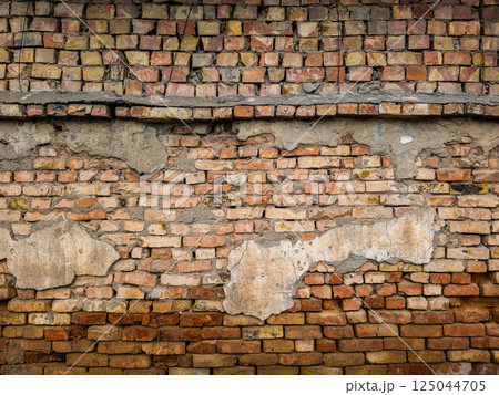 Old eroded brick wall with damaged plaster leftovers Old eroded brick wall with damaged plaster leftovers 125044705