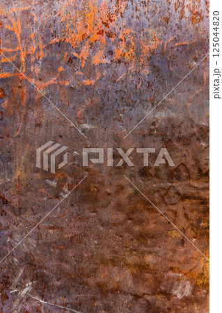 Heavily rusted metal surface with remnants of orange paint, showing deep corrosion and texture. 125044820