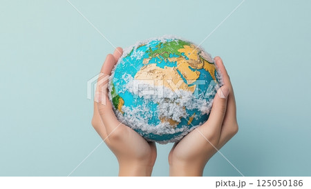 Hands holding a globe covered in clouds, symbolizing environmental awareness and climate change, showcasing the Earths continents and oceans. 125050186