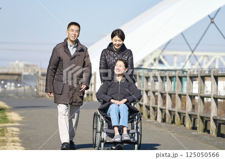 母親が乗る車椅子を押して散歩する家族 125050566