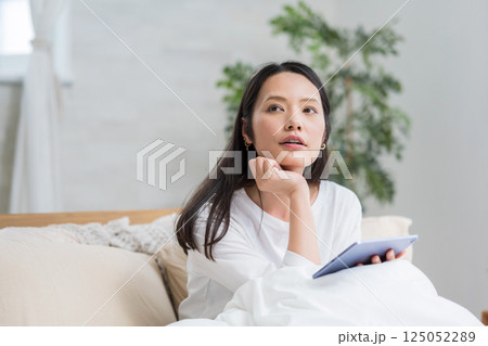 ベッドでタブレットを操作する女性｜読書勉強｜健康的な暮らしイメージ｜ウェルビー女子｜ウェルビーイング 125052289
