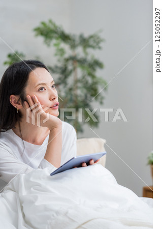 ベッドでタブレットを操作する女性｜読書勉強｜健康的な暮らしイメージ｜ウェルビー女子｜ウェルビーイング 125052297