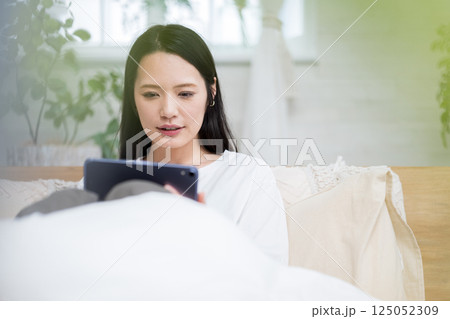 ベッドでタブレットを操作する女性｜読書勉強｜健康的な暮らしイメージ｜ウェルビー女子｜ウェルビーイング 125052309