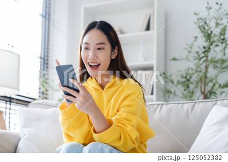 Happy young asian woman relax on comfortable couch at home texting messaging on smartphone 125052382