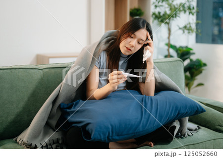 Young Asian woman suffering from flu symptoms, covered with a blanket on a sofa. Concept of illness, healthcare, 125052660
