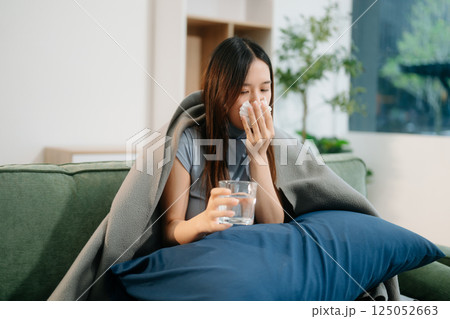 Young Asian woman suffering from flu symptoms, covered with a blanket on a sofa. Concept of illness, healthcare, 125052663