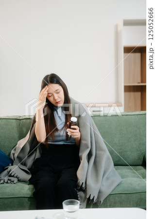 Young Asian woman suffering from flu symptoms, covered with a blanket on a sofa. Concept of illness, healthcare, Young Asian woman suffering from flu symptoms, covered with a blanket on a sofa. Concept of illness, healthcare, 125052666