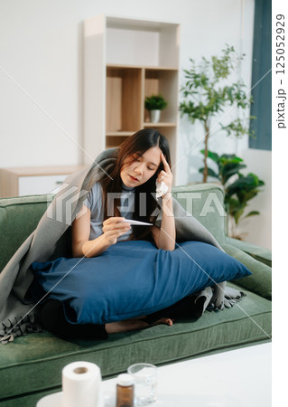 Young Asian woman suffering from flu symptoms, covered with a blanket on a sofa. Concept of illness, healthcare, Young Asian woman suffering from flu symptoms, covered with a blanket on a sofa. Concept of illness, healthcare, 125052929