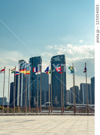 Flags of various nations wave in front of modern skyscrapers. 125054003
